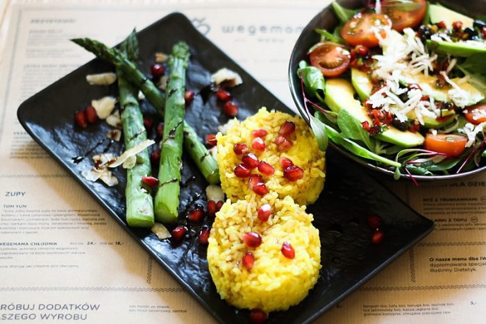 Photo of a delicious vegan meal with asparagus, apple and arugula salad, saffron rice, and pomegranate. 